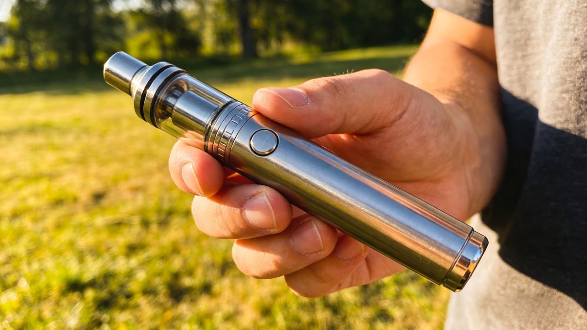 A person holding a durable metallic vape pen outdoors