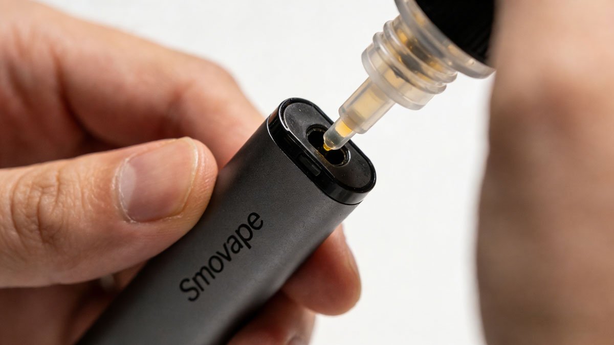 A person carefully filling a Smovape pod with e-liquid from a bottle, showing the fill port.