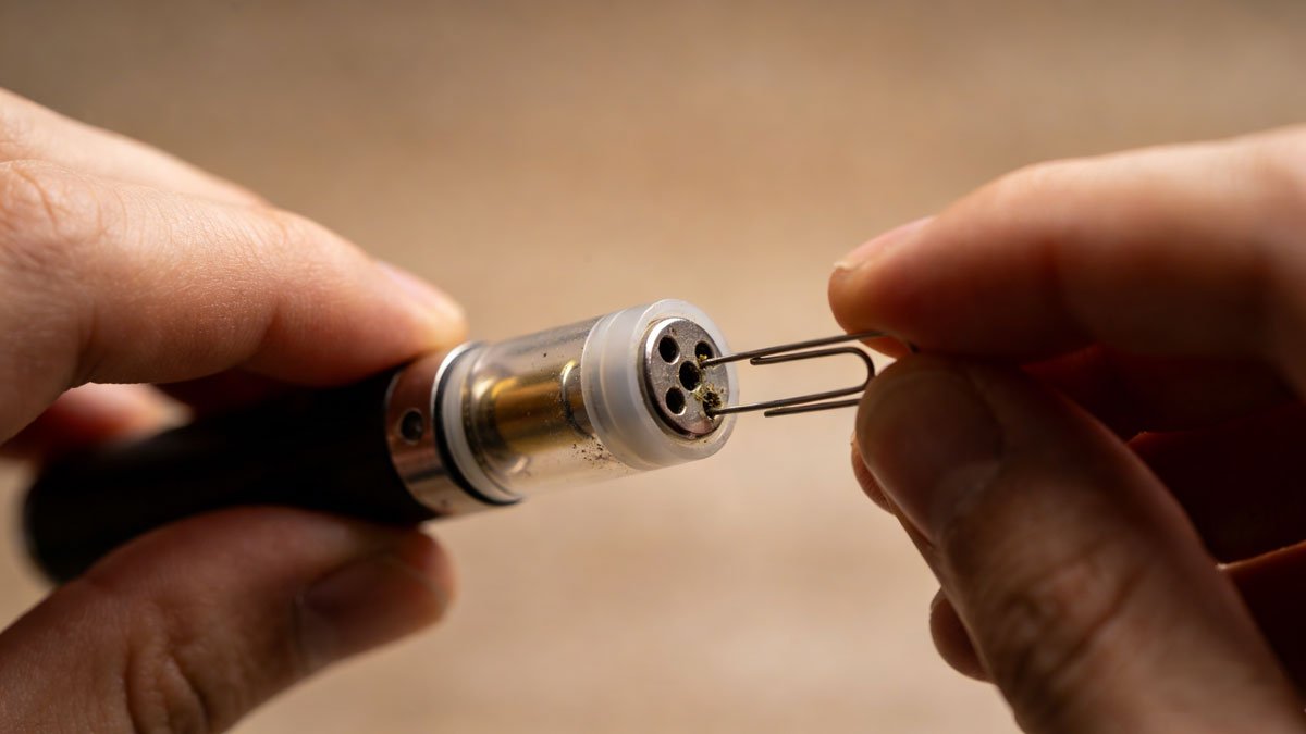 A person troubleshooting a clogged 510 vape cartridge with a paperclip.