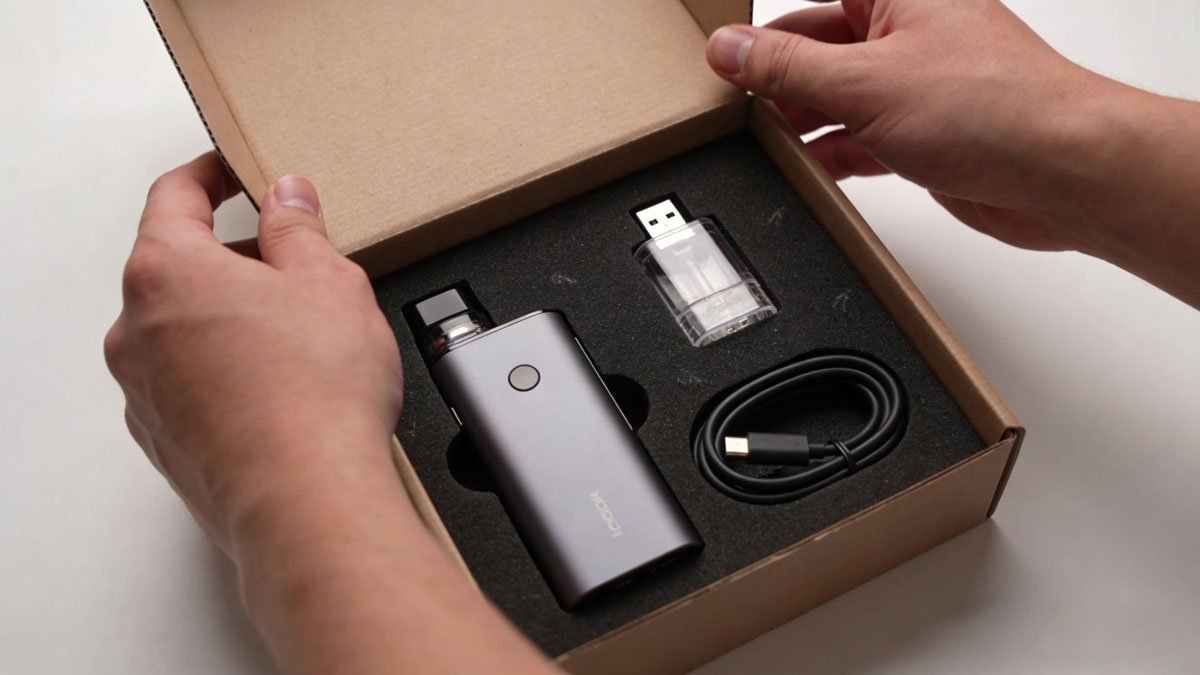 A person unboxing a vape starter kit, showing the contents which include the device, pod, and a charging cable.